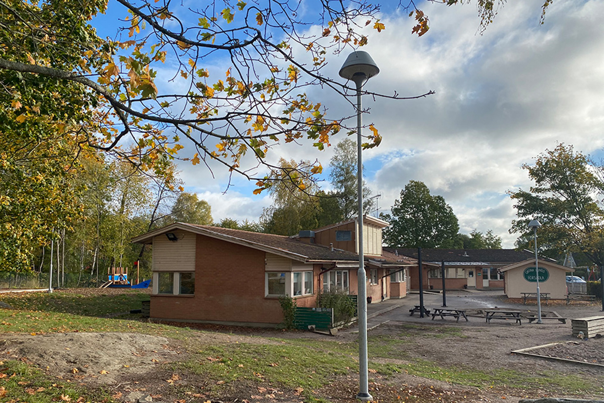 En låg tegelbyggnad med tak av tegel. Träd och gräsmatta finns framför förskolebyggnaden.