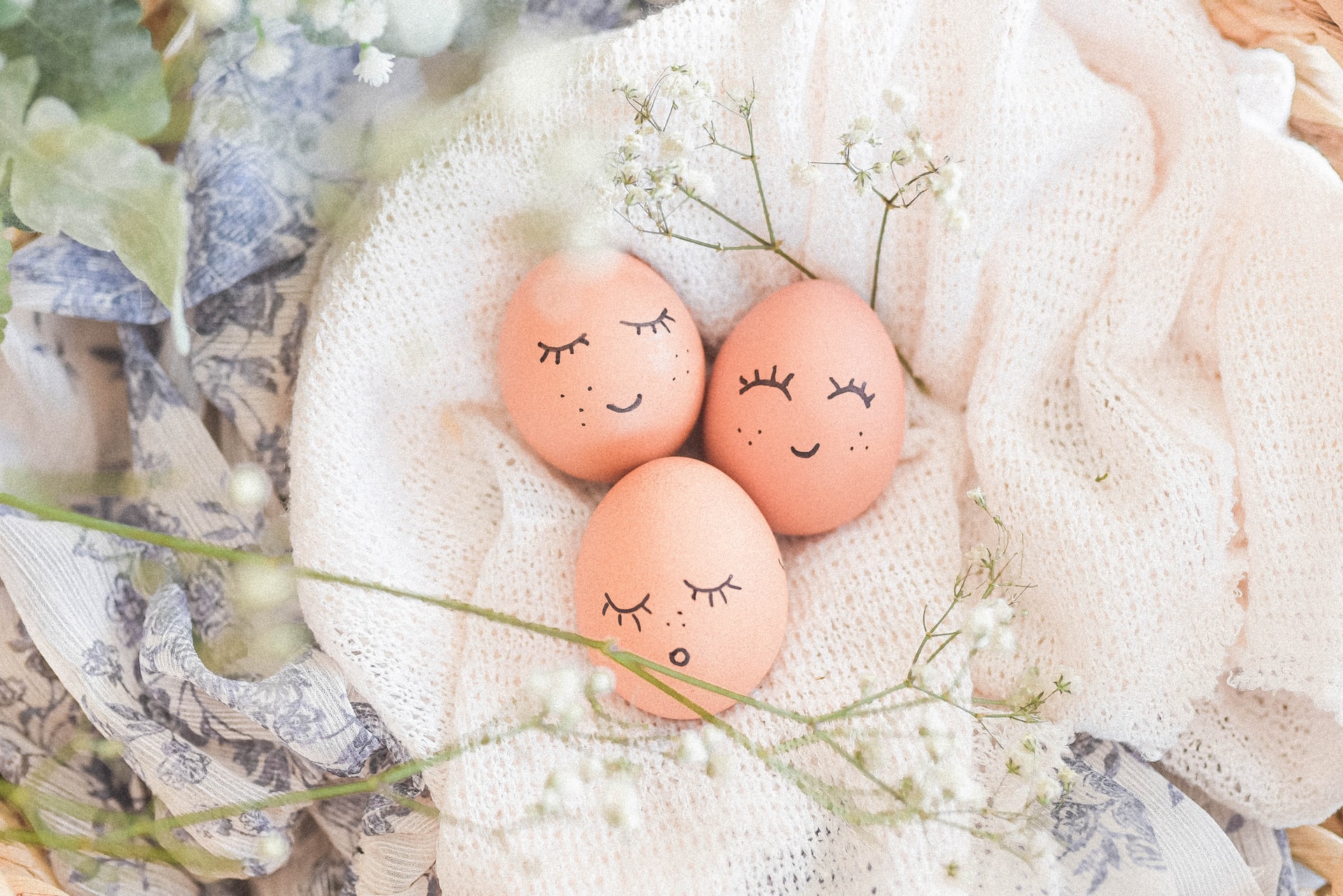 Tre rosa ägg med målade glada ansikten. Äggen ligger på en vit filt.