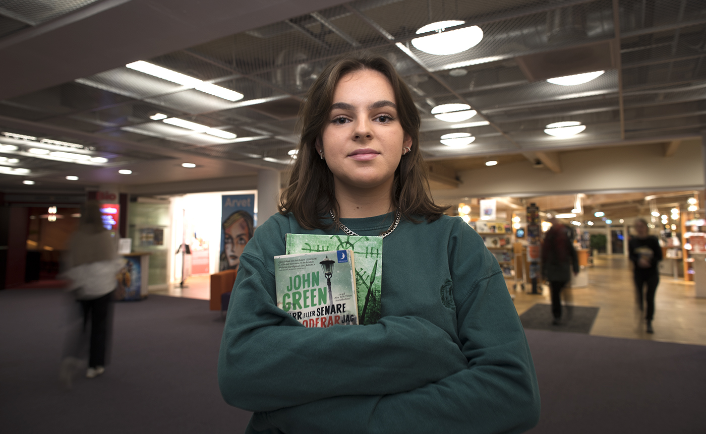 En ung tjej håller i två böcker framför biblioteket. 