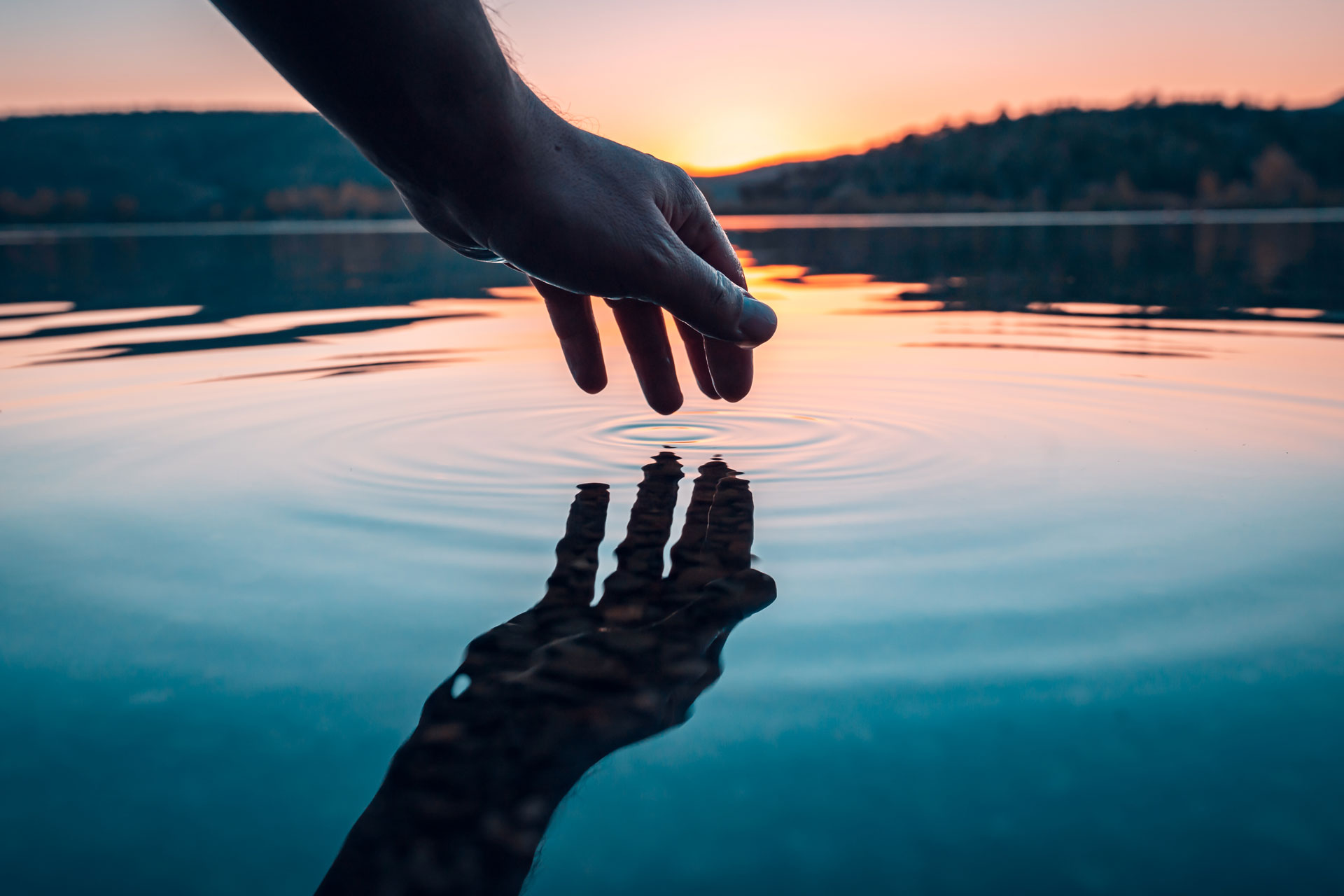 En hand som rör vattenytan på en sjö