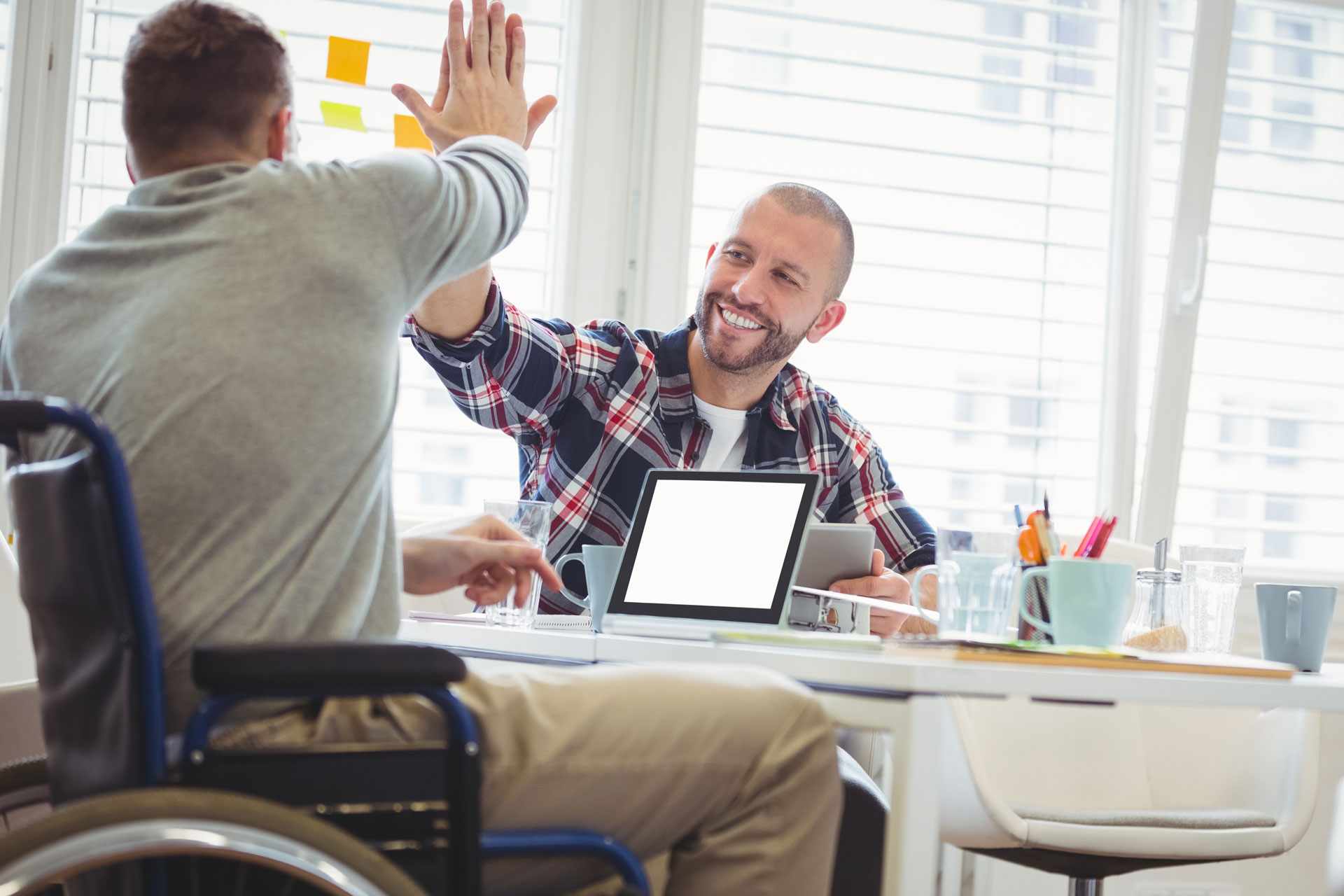 En rullstolsbunden man gör high five med en kille. De sitter vid ett skrivbord med blanketter.