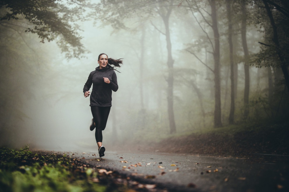 En kvinna joggar på en dimmig väg.