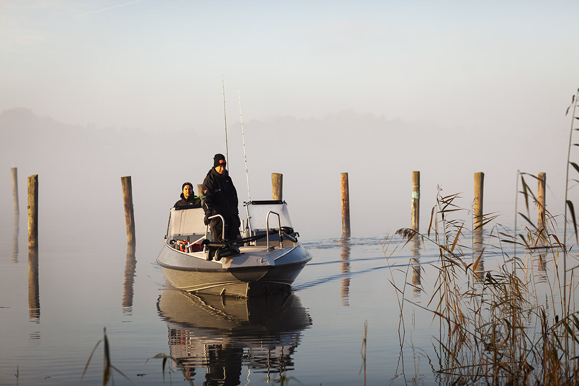 Två killar är i en fiskebåt en tidig och dimmig morgon.