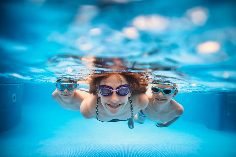 Tre barn simmar under vattnet i en pool.