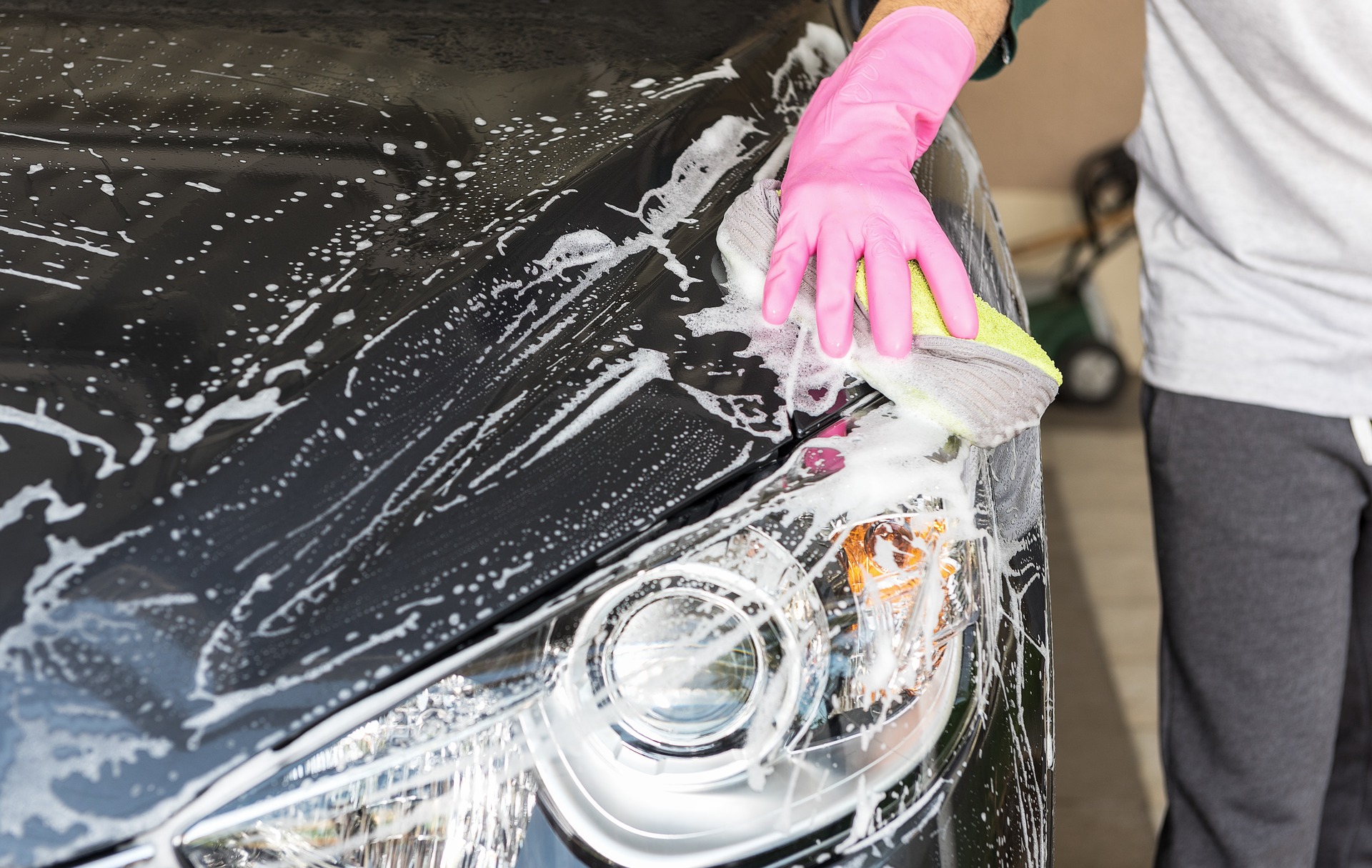 En person med rosa skyddshandskar tvättar en bil med en svamp. Personen är inomhus.