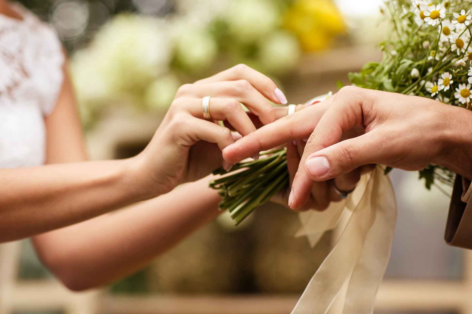 Två händer som håller blommor och trär på en ring.