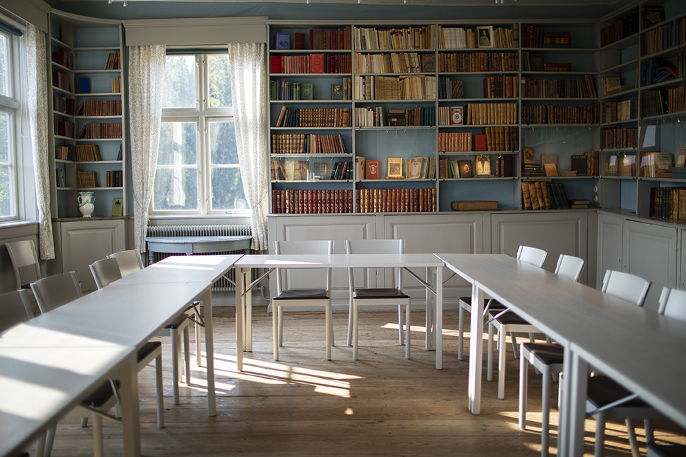 Konferensrum med långa, vita bord och stolar. Böcker syns i bakgrunden.