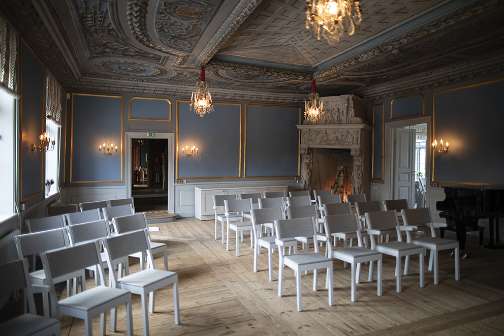 Konferensrum som är blått och massor av vita stolar står uppradade. En öppen spis syns i bakgrunden. Taket har en takmålning och några kristallkronor.