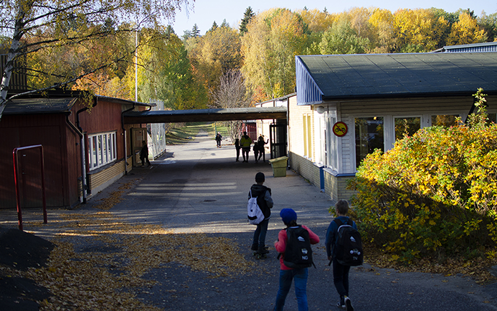 Ekebyhovsskolan.Några elever går mot skolgården. Skolan ligger till vänster i bild och till höger ser man matsalen.