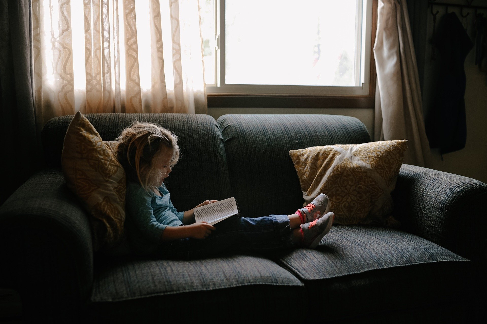 Barn läser bok i soffan.