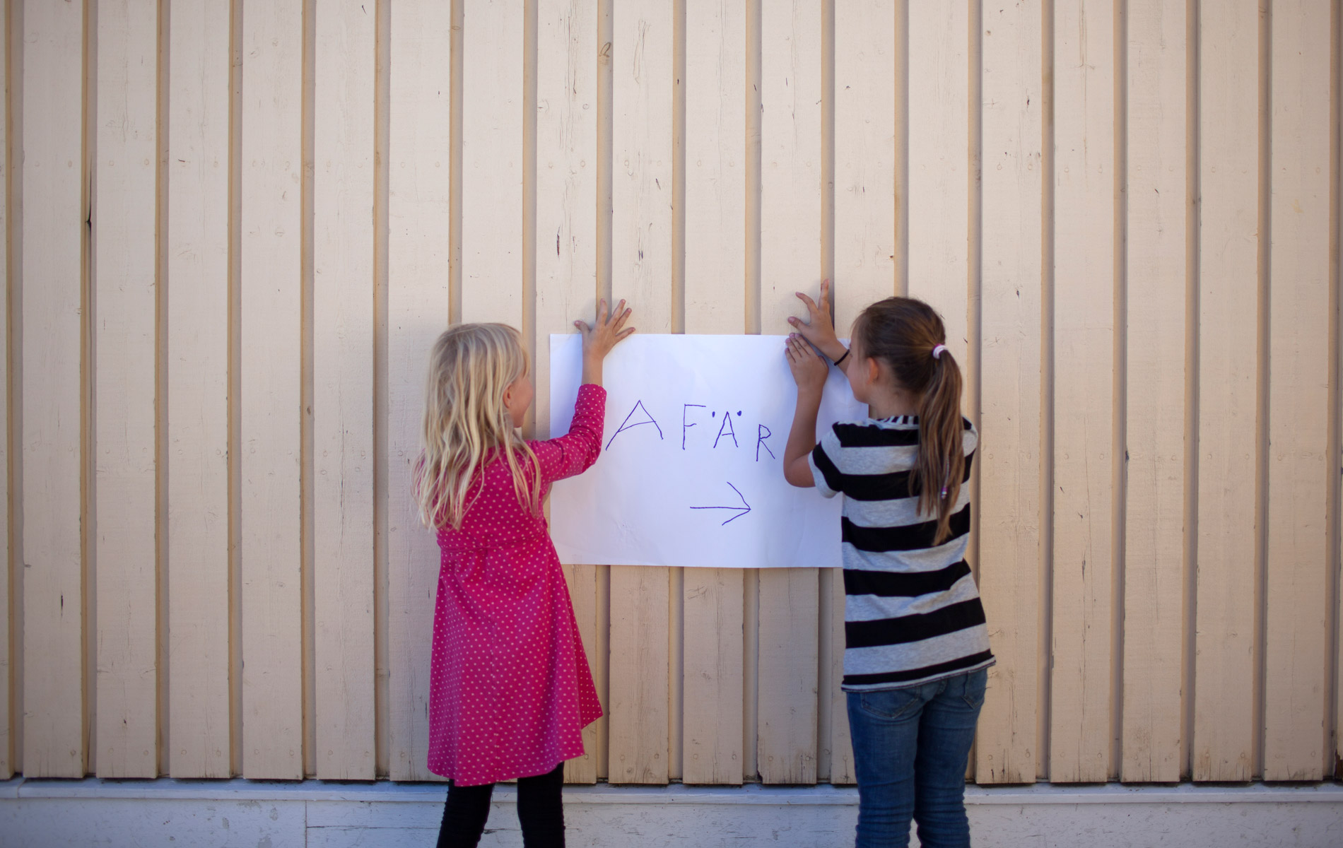 Två barn som håller upp en skylt med texten affär mot en vägg.