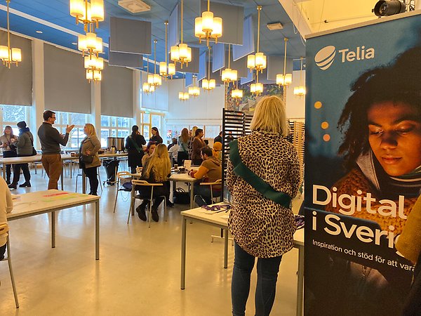 Foto från evenemanget med Telias reklamskylt och värd
från Ekerö kommun i förgrunden. Övriga deltagare i bakgrunden. 
