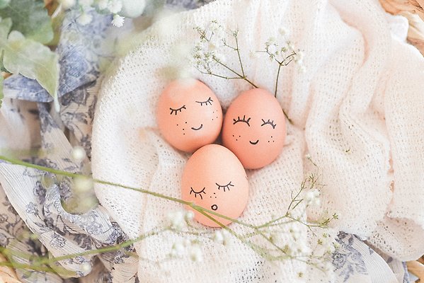 Tre rosa ägg med målade glada ansikten. Äggen ligger på en vit filt.