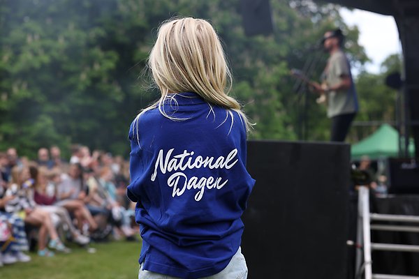 En liten flicka står med en blå t-shirt där det står Nationaldagen på ryggen. I bakgrunden syns publik och Robin Bengtsson
