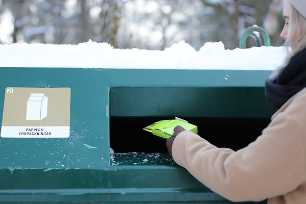 Kvinna som slänger förpackning i grön container.